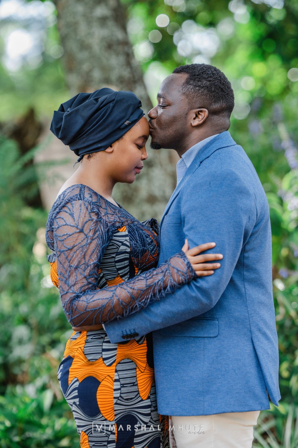 Couple in blue and traditional attire sharing a gentle forehead kiss